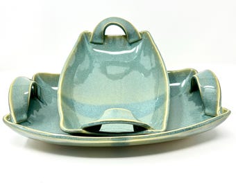 May include: A set of three ceramic serving dishes in a light blue glaze with a yellow rim. The dishes have unique handles and are nested together.