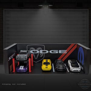 May include: A miniature garage diorama featuring several toy Dodge cars. The cars are in various colors, including silver, yellow, black, and white. The garage backdrop has the Dodge logo and SRT branding. The display is set against a dark background.