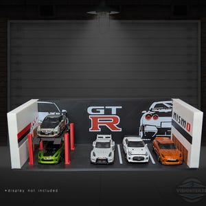 May include: A diorama featuring miniature model cars, including silver, green, white, and orange vehicles. The backdrop includes the text "GT-R" and a garage door. The display is framed by white structures with red stripes.