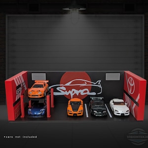 May include: A miniature garage diorama with a black backdrop and red accents. The garage features a Supra logo and a Toyota logo. Five toy cars are parked inside, including an orange car on a lift and a white car.