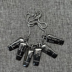May include: A silver-toned necklace featuring five rectangular pendants. Each pendant has engraved scientific formulas and the number "0000". The chain is a delicate, coiled design.