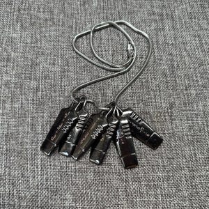 May include: A silver-toned necklace featuring six rectangular pendants. Each pendant has a unique design with etched lines and mathematical equations. The necklace chain is a thin, coiled design. The pendants are arranged on a gray fabric surface.