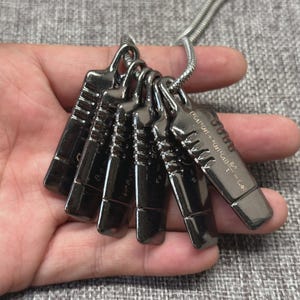 May include: A silver-toned necklace featuring six rectangular pendants. Each pendant has a unique design with etched lines and numbers. One pendant displays mathematical symbols. The necklace is on a silver chain.