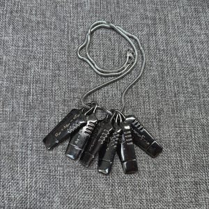 May include: A silver-toned necklace featuring a series of dark gray rectangular pendants. Each pendant has etched designs and symbols, with a silver chain. The pendants are arranged in a fan shape.