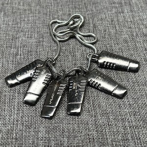 May include: A collection of silver-toned pendant necklaces. Each pendant has a rectangular shape with engraved mathematical symbols and equations. The necklaces are displayed on a gray textured surface.