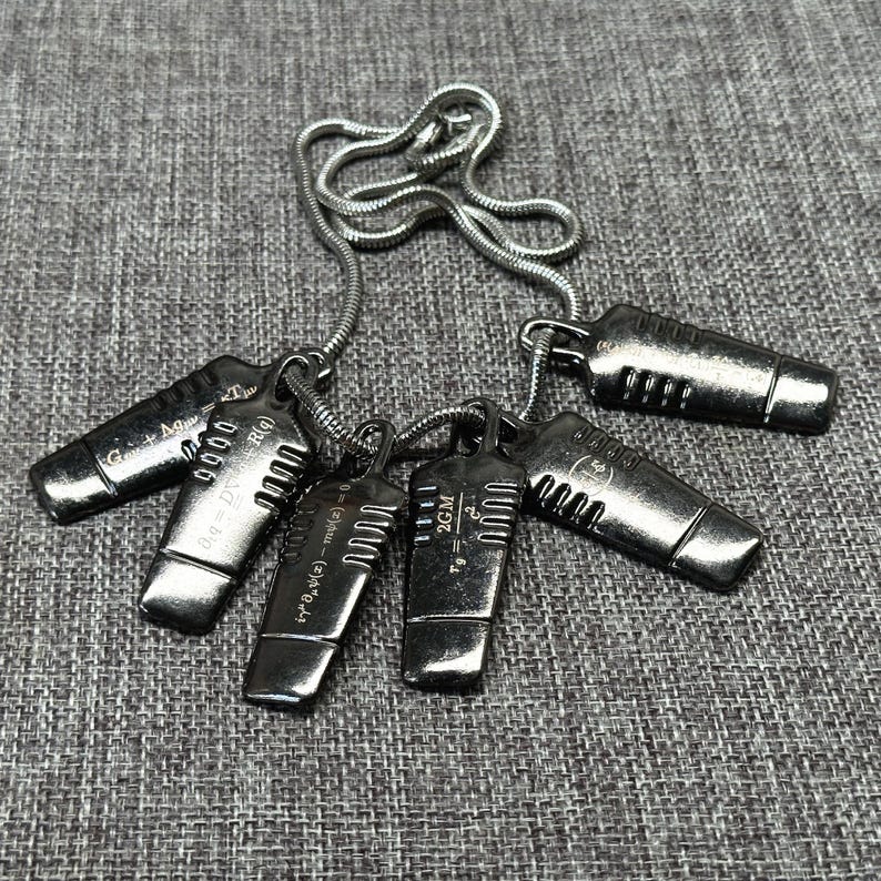 May include: A collection of silver-toned pendant necklaces. Each pendant has a rectangular shape with engraved mathematical symbols and equations. The necklaces are displayed on a gray textured surface.