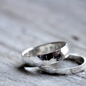 May include: Two silver hammered wedding bands stacked on top of each other. The bands are smooth and have a shiny finish.