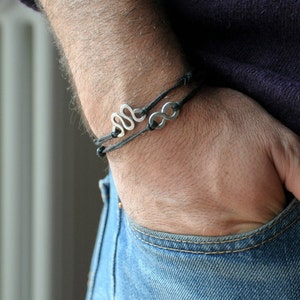 May include: A black leather bracelet with two silver charms, one shaped like a snake and the other like an infinity symbol.