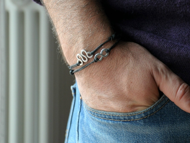 May include: A black leather bracelet with two silver charms, one shaped like a snake and the other like an infinity symbol.