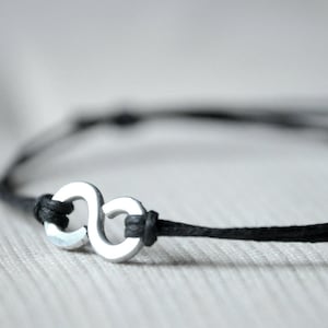 May include: A black cord bracelet with a silver infinity symbol charm.