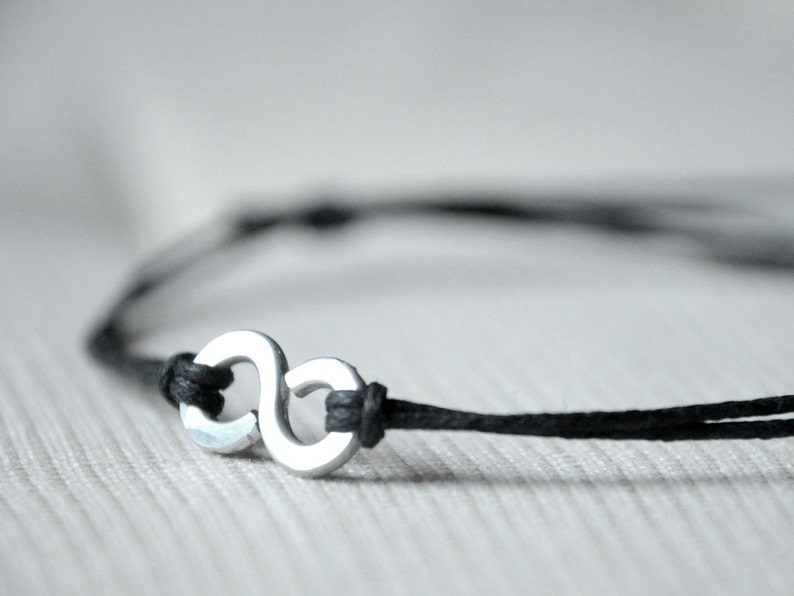 May include: A black cord bracelet with a silver infinity symbol charm.