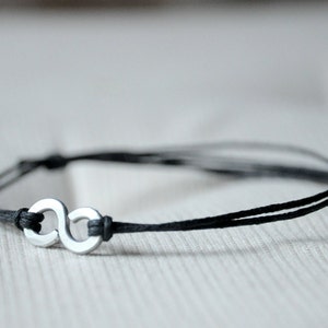May include: A black cord bracelet with a silver infinity symbol charm.