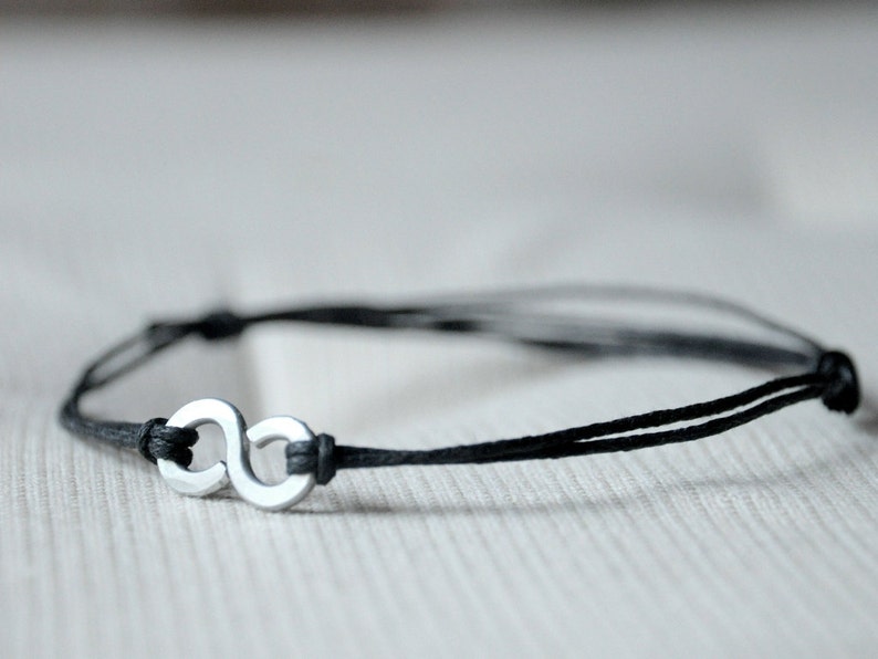 May include: A black cord bracelet with a silver infinity symbol charm.