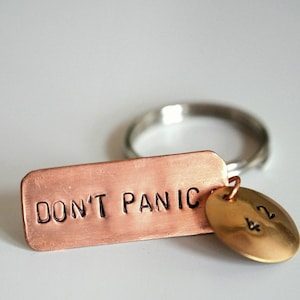 May include: A copper keyring with the words "Don't Panic" engraved on a rectangular tag. A small gold charm with the number "42" is attached to the keyring.