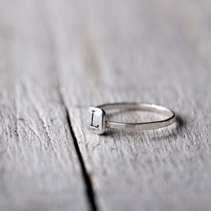 Peut inclure: Une bague en argent avec une bande carrée et la lettre "L" gravée sur le dessus.