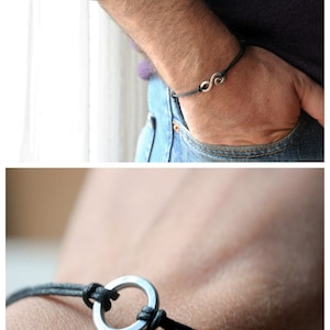 May include: A black leather bracelet with a silver circle charm. The bracelet is tied with a knot and has a simple design.