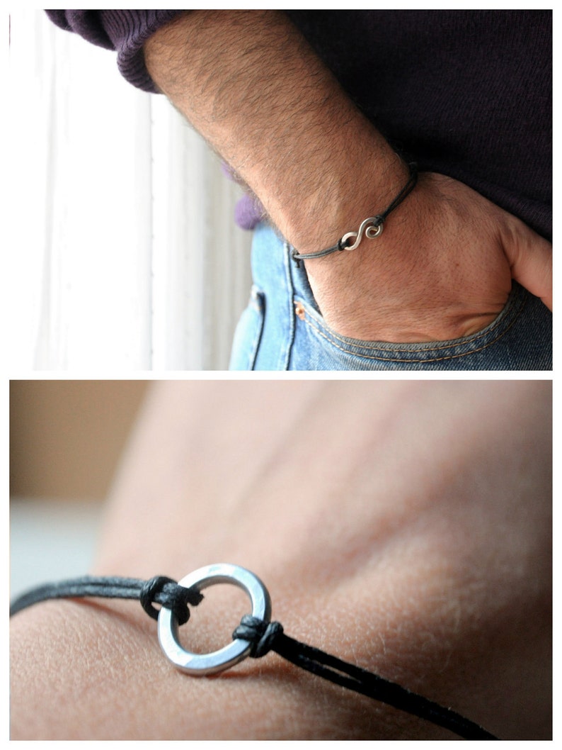 May include: A black leather bracelet with a silver circle charm. The bracelet is tied with a knot and has a simple design.