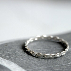 Peut inclure: Une bague en argent tressée sur une surface texturée grise.