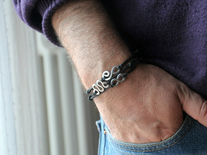 May include: A black leather bracelet with a silver charm featuring a stylized design of multiple loops.