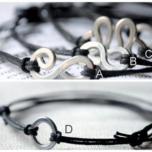 May include: Two black cord bracelets with silver metal charms. One bracelet has a charm shaped like a treble clef, the other has a round charm.