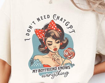 May include: Cream-colored t-shirt with a retro-style graphic of a woman with a red bow and a lollipop. The text on the shirt reads "I DON'T NEED CHATGPT MY BOYFRIEND KNOWS everything."