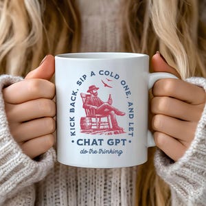 Könnte beinhalten: Weiße Keramik-Tasse mit humorvollem Design. Die Tasse zeigt eine sitzende Figur mit einer Flasche, einem Fass und dem Text "KICK BACK, SIP A COLD ONE, AND LET CHAT GPT do the thinking." Das Design ist in Rot und Blau.