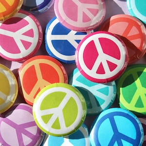 Könnte beinhalten: Eine Sammlung bunter Peace-Zeichen-Knöpfe. Die Knöpfe sind rund und haben ein weißes Peace-Zeichen auf verschiedenen farbigen Hintergründen, darunter Rot, Orange, Gelb, Grün, Blau, Lila und Pink.