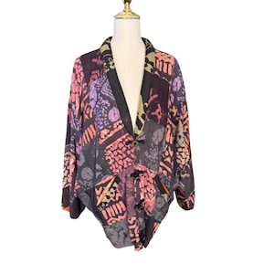 May include: A long-sleeve jacket featuring a dark base with a multi-colored patchwork pattern in shades of pink, purple, and tan. The jacket has a V-neckline, a wide collar, and three toggle closures down the front, with two visible pockets.