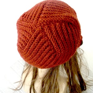 May include: A rust-colored crocheted beanie hat with a textured pattern. The hat is on a mannequin head with long brown hair.