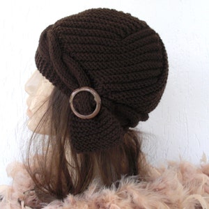 May include: A brown knitted hat with a decorative wooden circle accent. The hat has a slouchy, folded design.