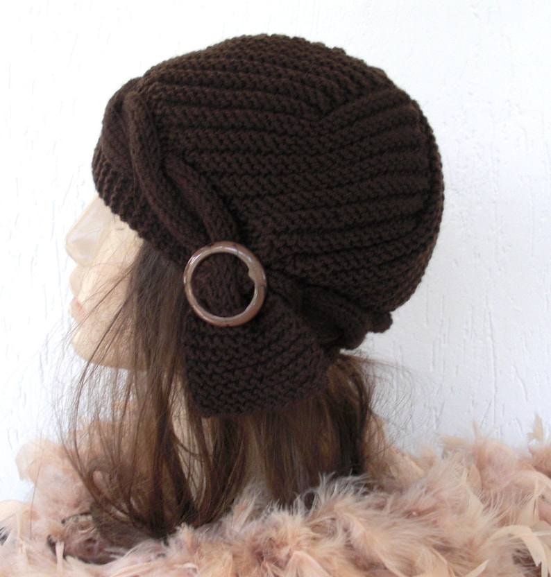 May include: A brown knitted hat with a decorative wooden circle accent. The hat has a slouchy, folded design.