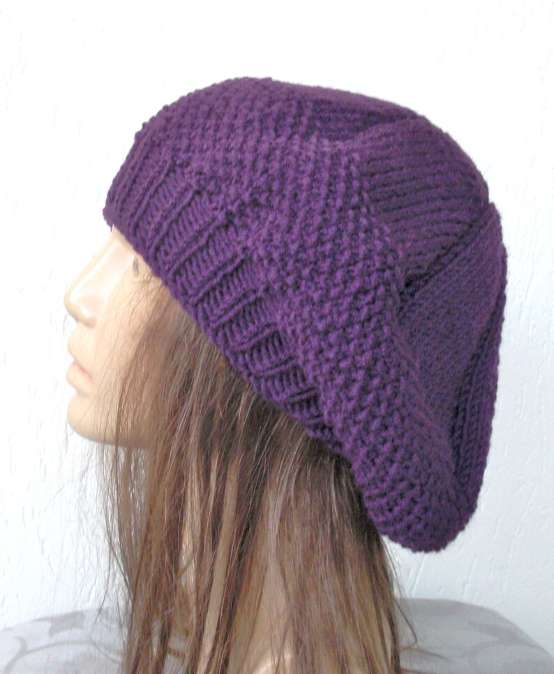May include: A purple knitted beanie hat with a slouchy fit. The hat is made of a soft, textured yarn.