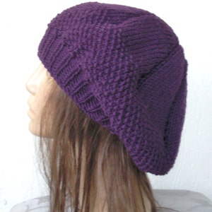 May include: A purple knitted beret with a textured pattern. The beret is worn on a mannequin with long brown hair.