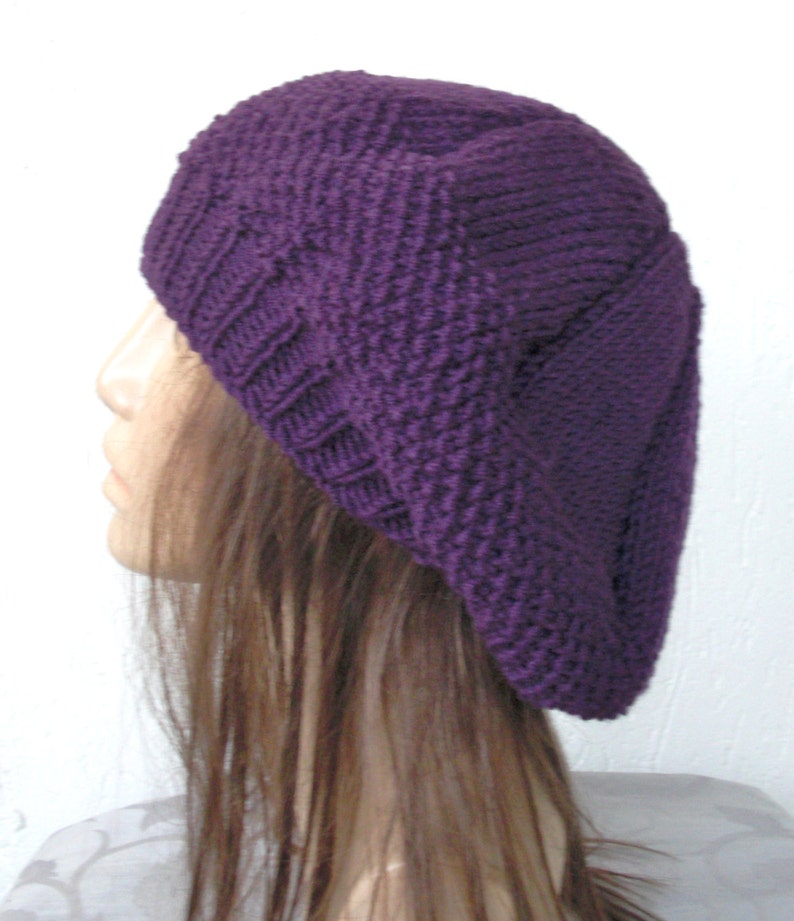 May include: A purple knitted beret with a textured pattern. The beret is worn on a mannequin with long brown hair.