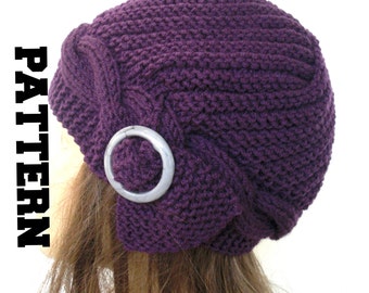 May include: Purple knitted hat with a decorative silver ring. The hat has a unique design with a folded brim.