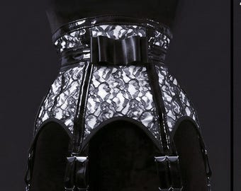 May include: A black and white lace garter belt featuring a glossy black patent trim, a central black bow detail at the waist, and four adjustable garter straps with metal clips attached to the bottom edge of the lace panel.