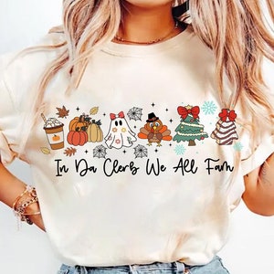 May include: Cream-colored long-sleeve shirt with a colorful graphic featuring a coffee cup, pumpkins, a ghost, a turkey, a Christmas tree, and a cookie. The text "In Da Clerb We All Fam" is printed below the graphic.