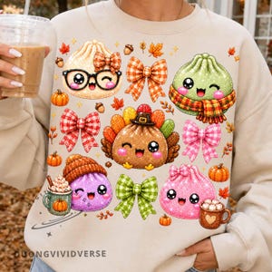 Puede incluir: Una sudadera de color beige con un estampado gráfico de varios alimentos antropomórficos y tiernos, incluyendo dumplings y un pavo, decorado con lazos de cuadros, hojas de otoño, bellotas y pequeñas tazas de chocolate caliente.