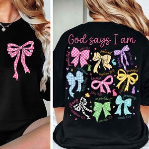 May include: Black t-shirt with a colorful bow design and the text "God says I am" with bible verses and words like "protected", "unique", "loved", "valued", "brave", "powerful", "strong", "important", and "precious".