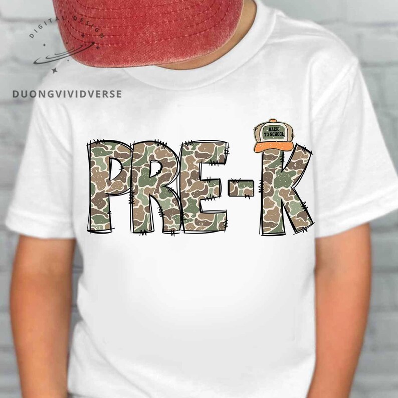 May include: A white t-shirt featuring the text PRE-K in a camouflage pattern with black stitched outlines. A small graphic of a baseball cap with the text BACK TO SCHOOL is positioned above the letter K. The design is centered on the chest.