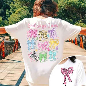 May include: White t-shirt with the text "God says I am" and a circle of colorful bows with bible verses. Each bow has a word describing a quality, such as "strong", "unique", "loved", "important", "precious", "valued", "protected", "peaceful", "joyful".
