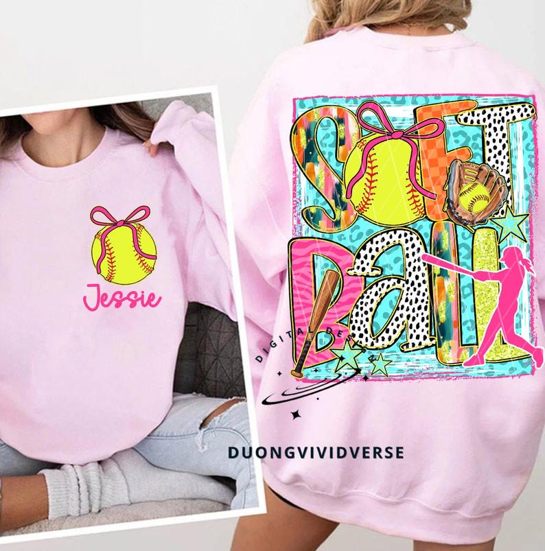May include: Pink sweatshirt with a colourful graphic design featuring a softball, a bat, and the word "Softball". The graphic also includes stars, animal print, and a silhouette of a player. The sweatshirt has the name "Jessie" printed on the front.