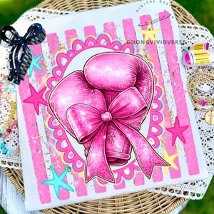May include: A white t-shirt featuring a graphic of a pink boxing glove adorned with a large pink bow, centered within a scalloped circular frame. The background displays vertical pink stripes, yellow and turquoise stars, and the text DUONGVIVIDVERSE.