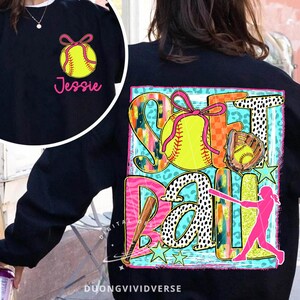 May include: Black sweatshirt with a colourful graphic design featuring the word "Softball" with a softball, bat, and a player. The design includes a variety of patterns, including leopard print, polka dots, and stripes. The text "Jessie" is on the front of the sweatshirt.