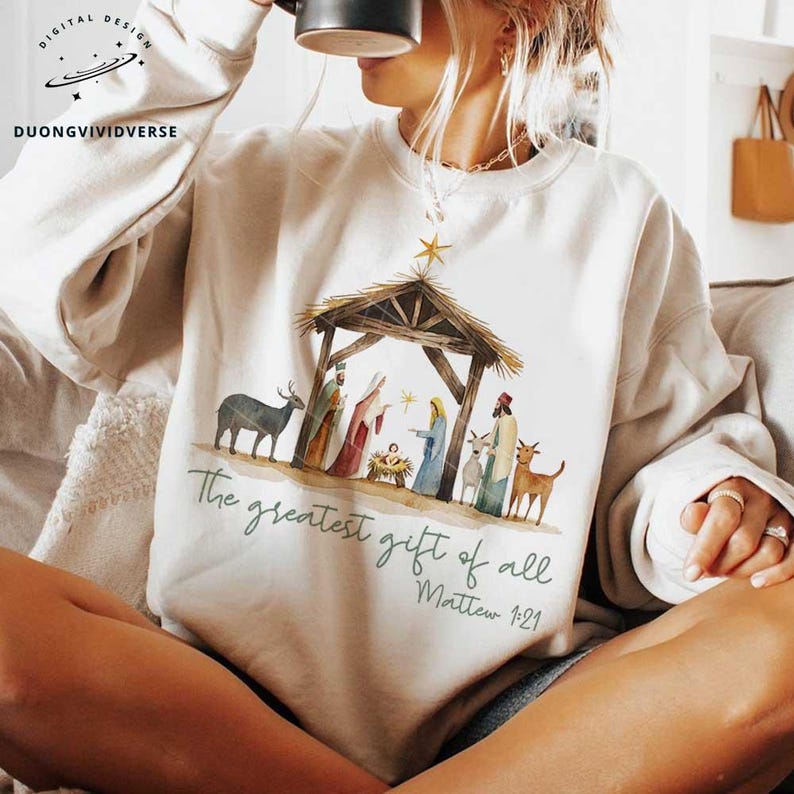 May include: A white sweatshirt with a watercolor illustration of the nativity scene. The text "The greatest gift of all Matthew 1:21" is printed below the image.