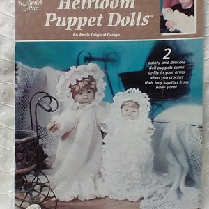 May include: A crochet pattern book titled "Heirloom Puppet Dolls" by Annie's Attic. The cover features two white crochet dolls with bonnets and a small inset photo. The text on the cover includes "CROCHET" and "An Annie Original Design."
