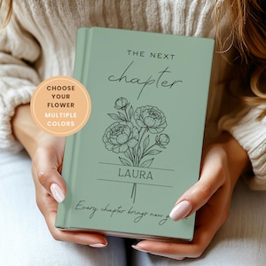 May include: A sage green hardcover journal featuring a black line art illustration of a flower bouquet. The text reads THE NEXT chapter, LAURA, and Every chapter brings new growth. A circular peach badge states CHOOSE YOUR FLOWER MULTIPLE COLORS.