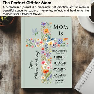 May include: A personalized journal with a floral cross design. The journal cover is light green and features the words "MOM IS" and inspirational words. The cross is adorned with colorful flowers and a dove. The text "Love, Olivia & Avery" is also present.