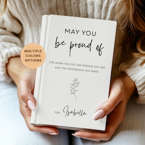 May include: A white journal with the text "MAY YOU be proud of THE WORK YOU DO, THE PERSON YOU ARE AND THE DIFFERENCE YOU MAKE" and the name "Isabella". A sticker on the side says "MULTIPLE COLORS OPTIONS".