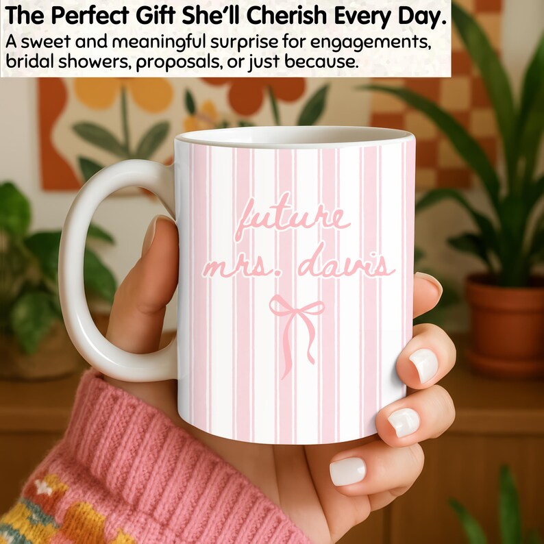 Pink Future Mrs. mug with cute pastel coquette bow and vertical stripes, personalized with future last name. Shown in cozy indoor scene as a sweet bride-to-be gift for engagements, bridal showers, and wedding celebrations. Aesthetic personalized ceramic mug perfect for daily use and wedding planning mornings.